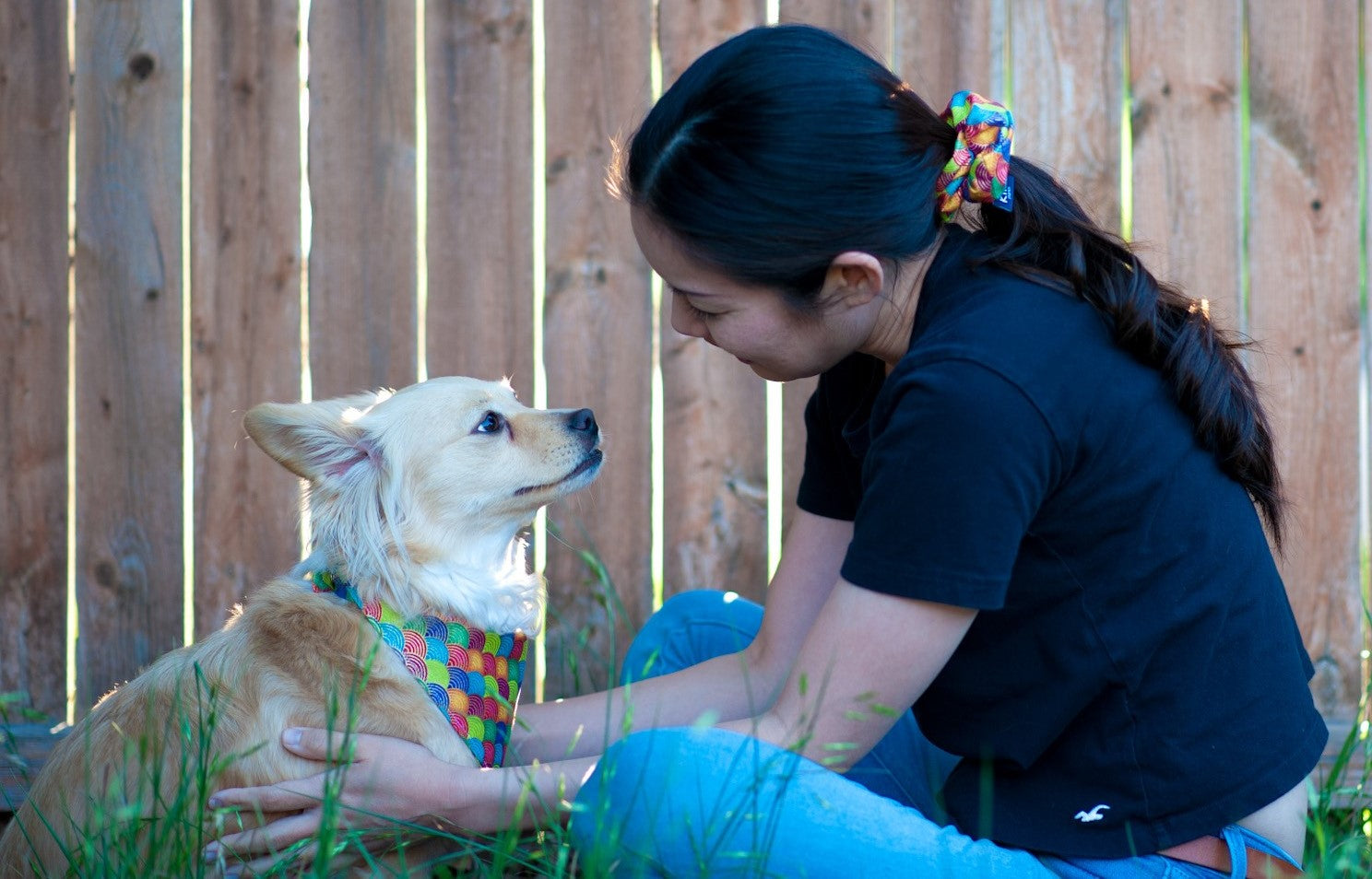 Rie, the founder of KIKI Japan, sitting outdoors with her dog, Kiki. Rie is wearing a scrunchie from KIKI Japan, while Kiki is wearing a rainbow traditional Japanese pattern pet bandana from KIKI Japan.